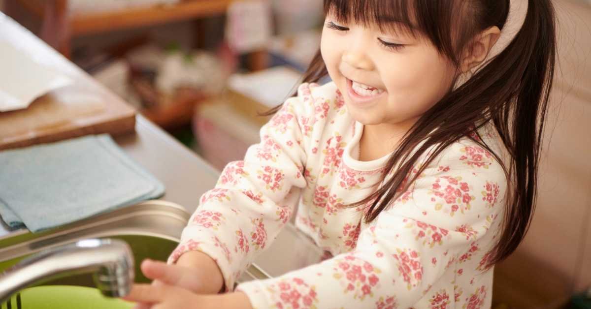 child after washing lunch box at kitchen sink