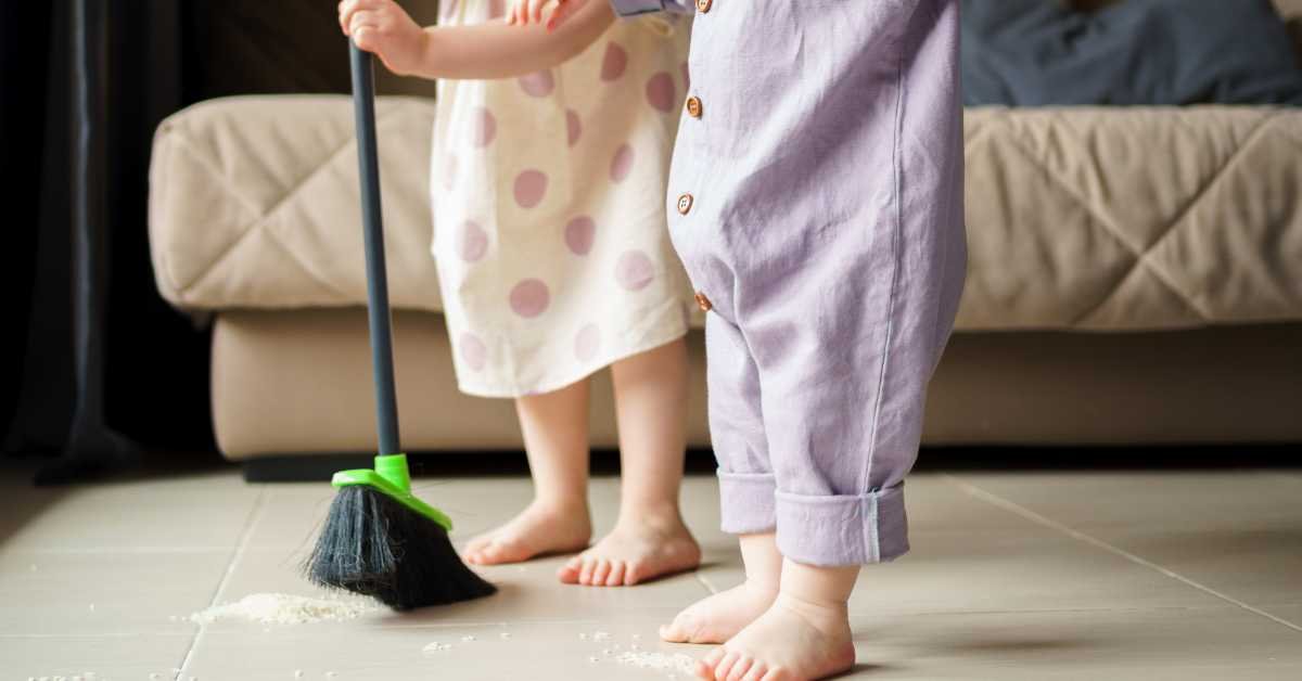 child sweeping floor at home with broom